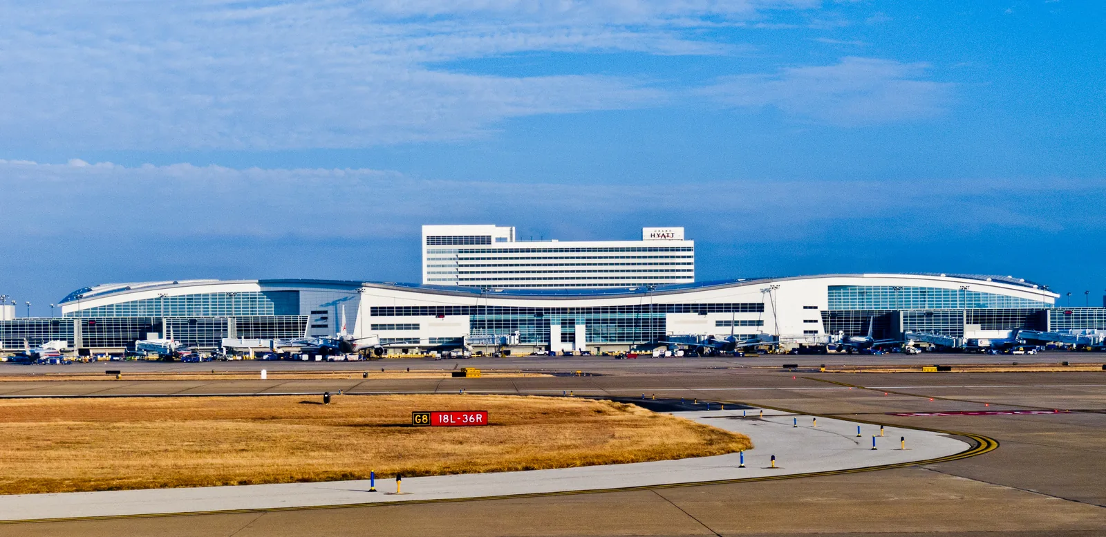 Terminal D at Dallas Fort Worth, its glass frontage running the length of the picture with the airport hotel rising behind it.