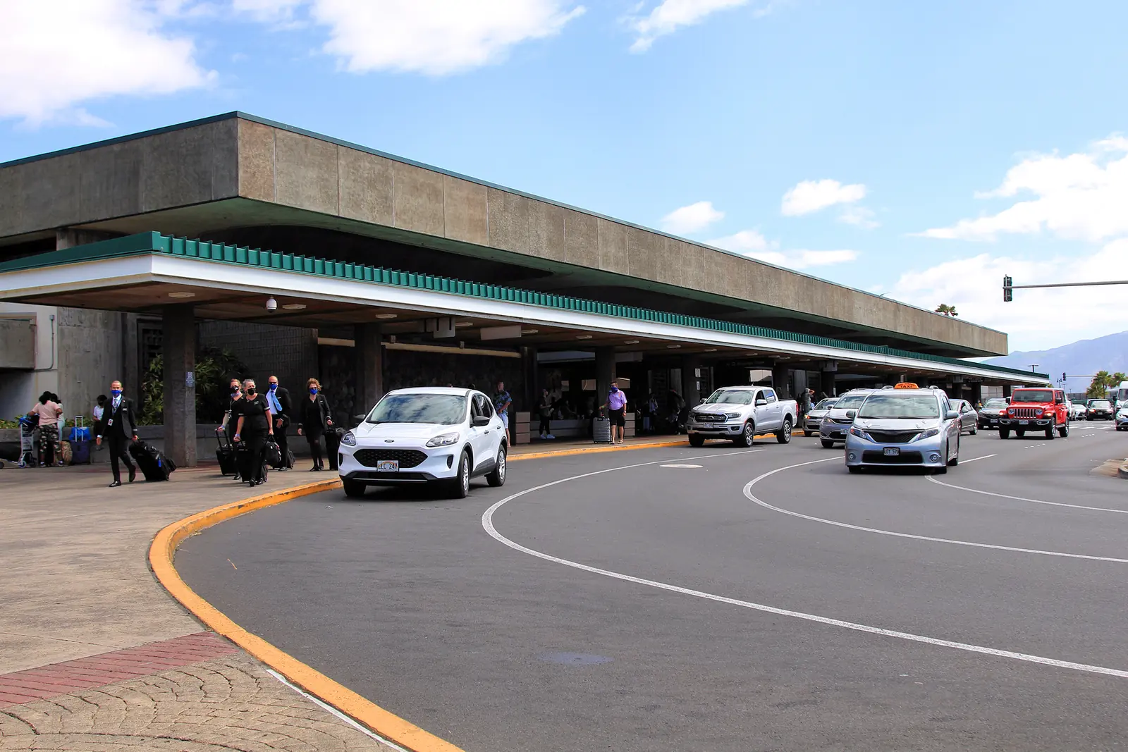 The kerb outside the terminal at Kahului Airport on Maui, with cars pulled up under the overhang.