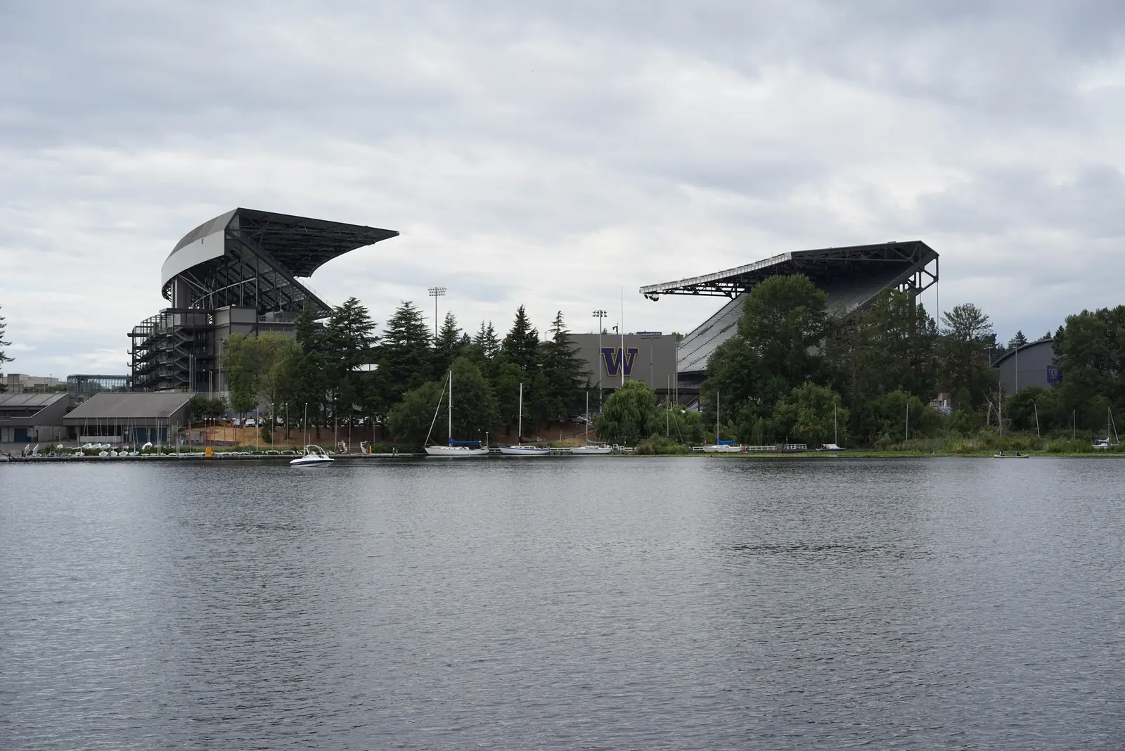 Husky Stadium seen across Union Bay, with sailboats moored along the shore below the stands.