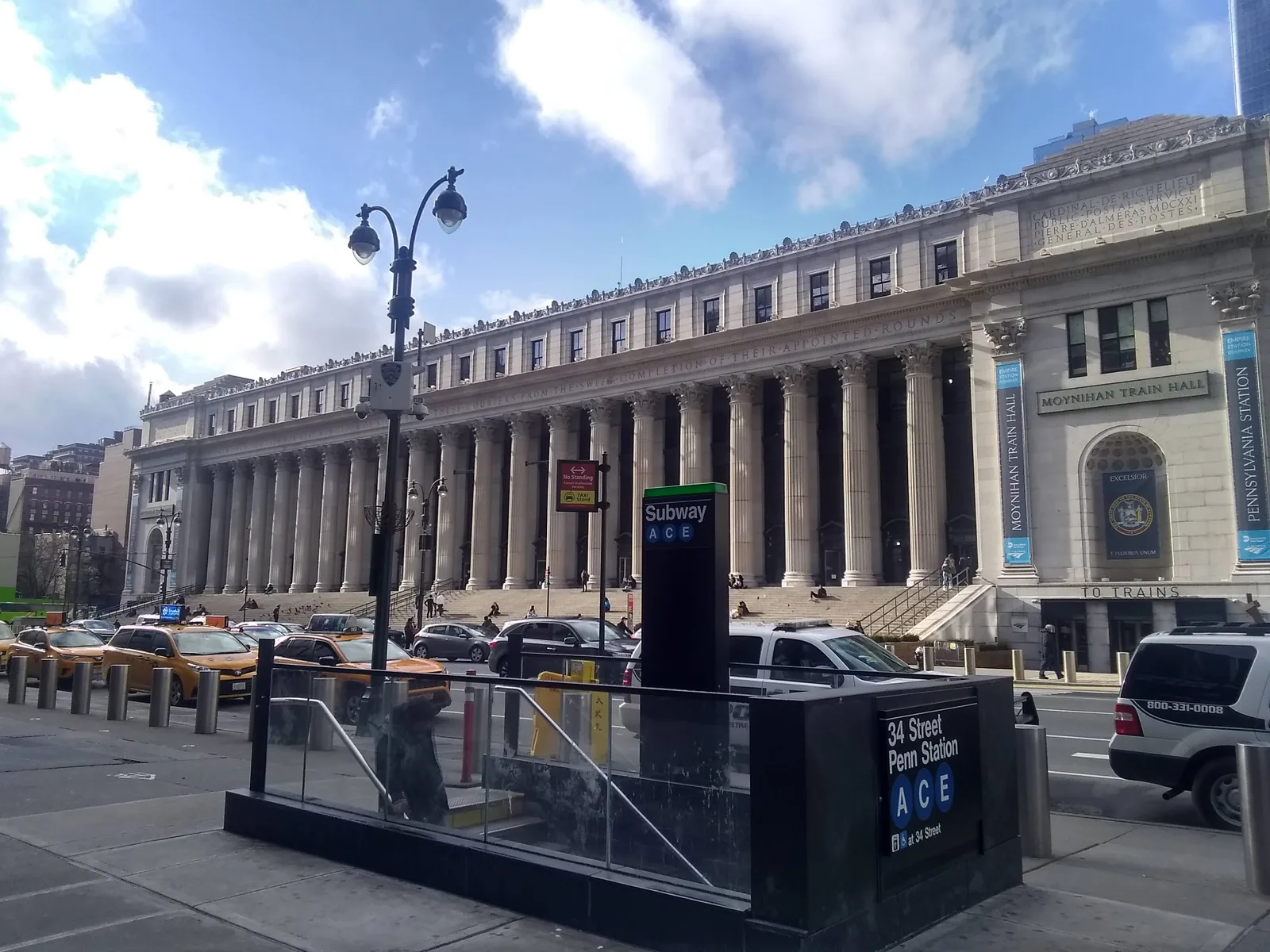 The colonnade of the Farley Building on Eighth Avenue, where Moynihan Train Hall is, with a Penn Station subway entrance in front of it.